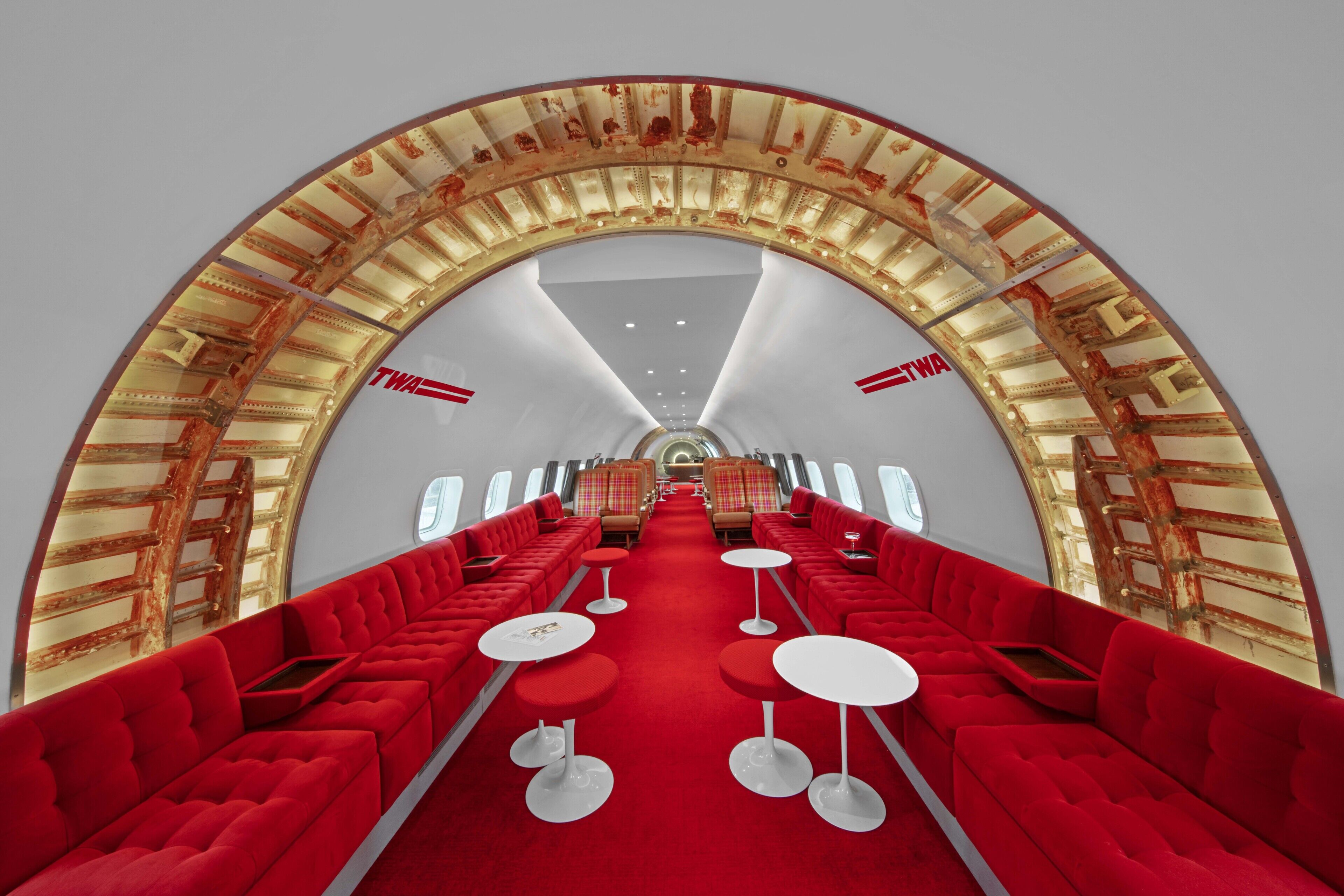 A luxurious airplane interior with red seating, a central aisle, and overhead compartments.