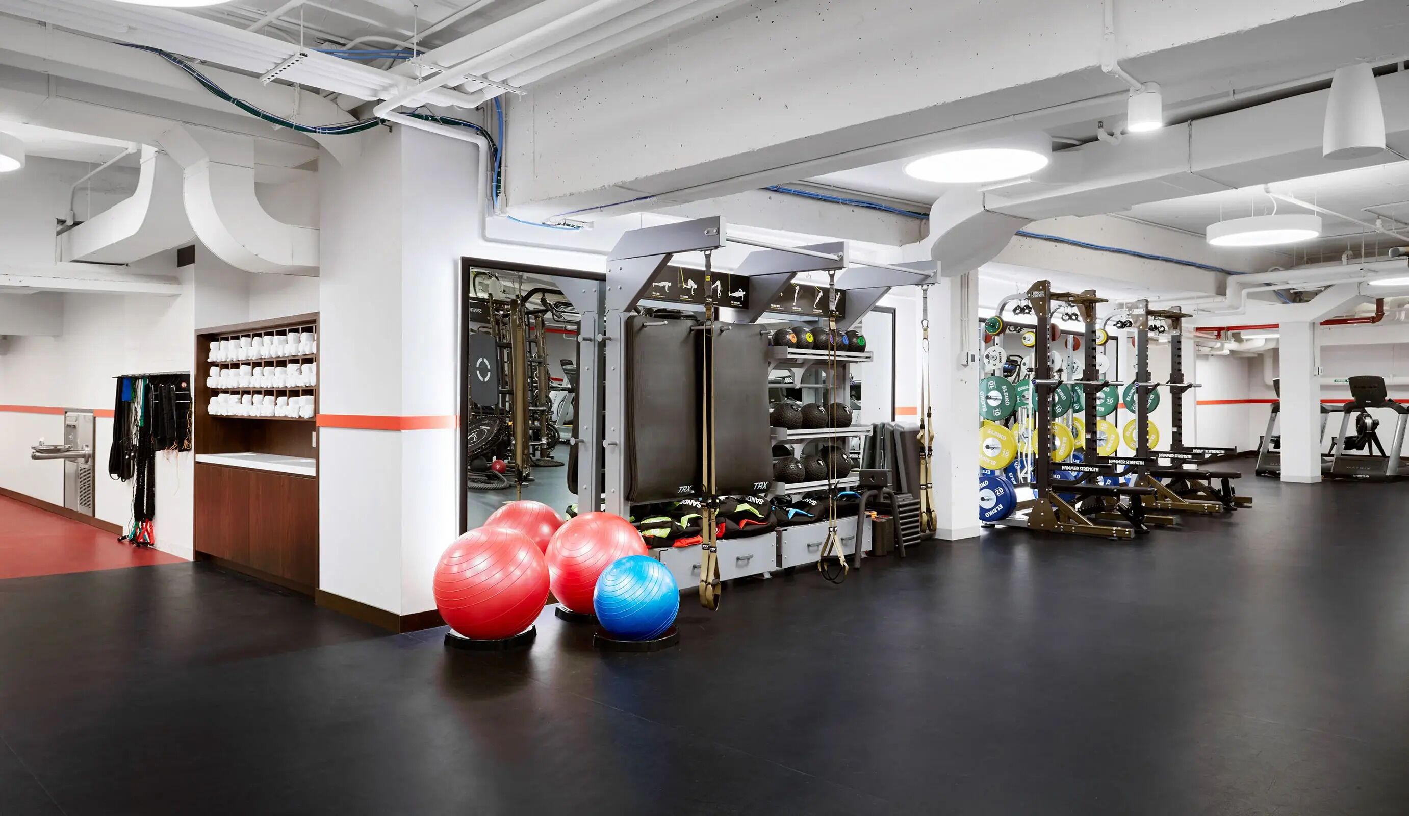 Et fitnessrum med styrketræningsudstyr, træningsbolde og en vandstation.