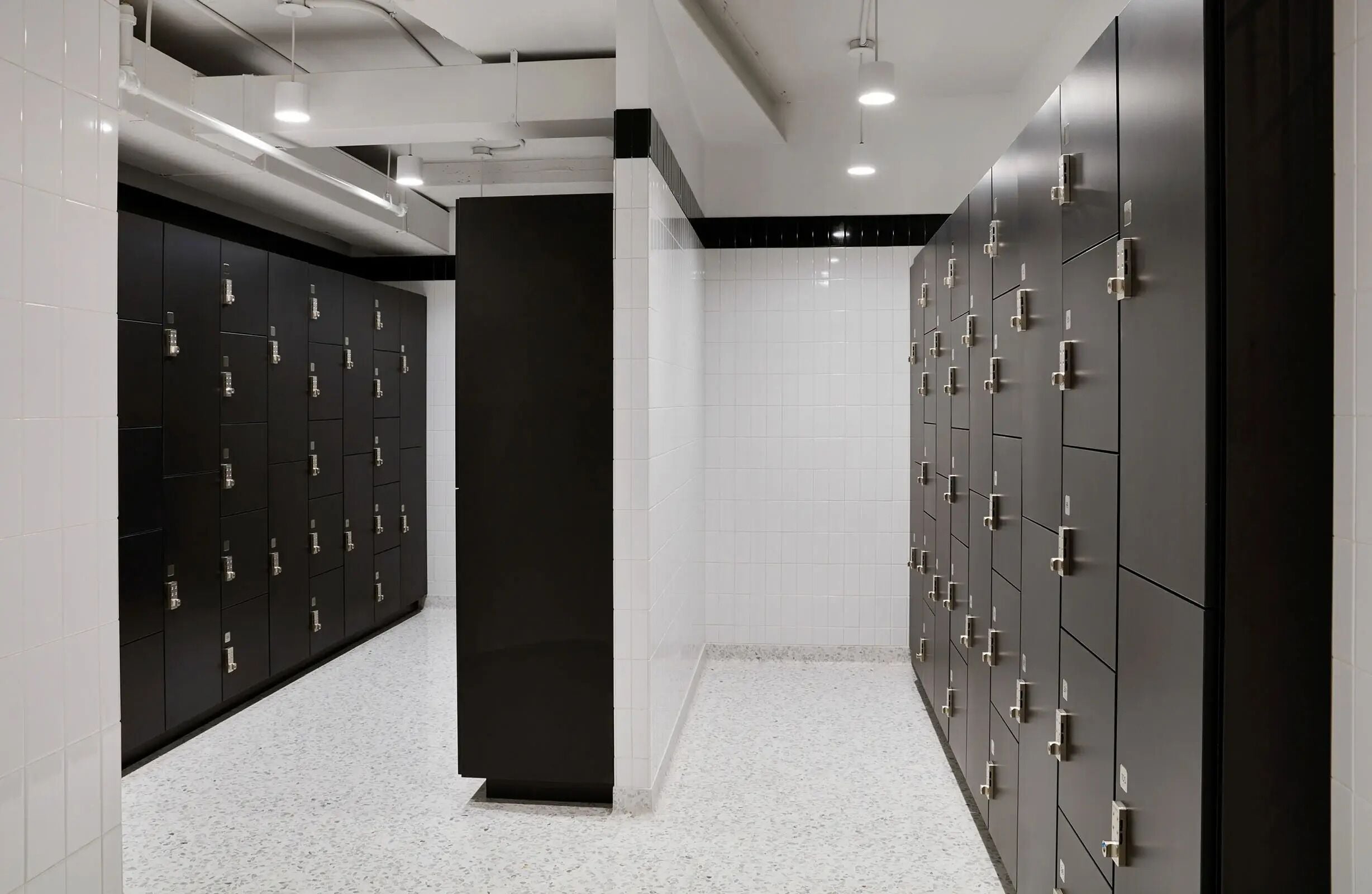 A modern locker room with multiple lockers on both sides, a central pillar, and a tiled floor.