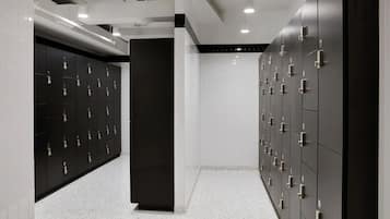 A modern locker room with multiple lockers on both sides, a central pillar, and a tiled floor.