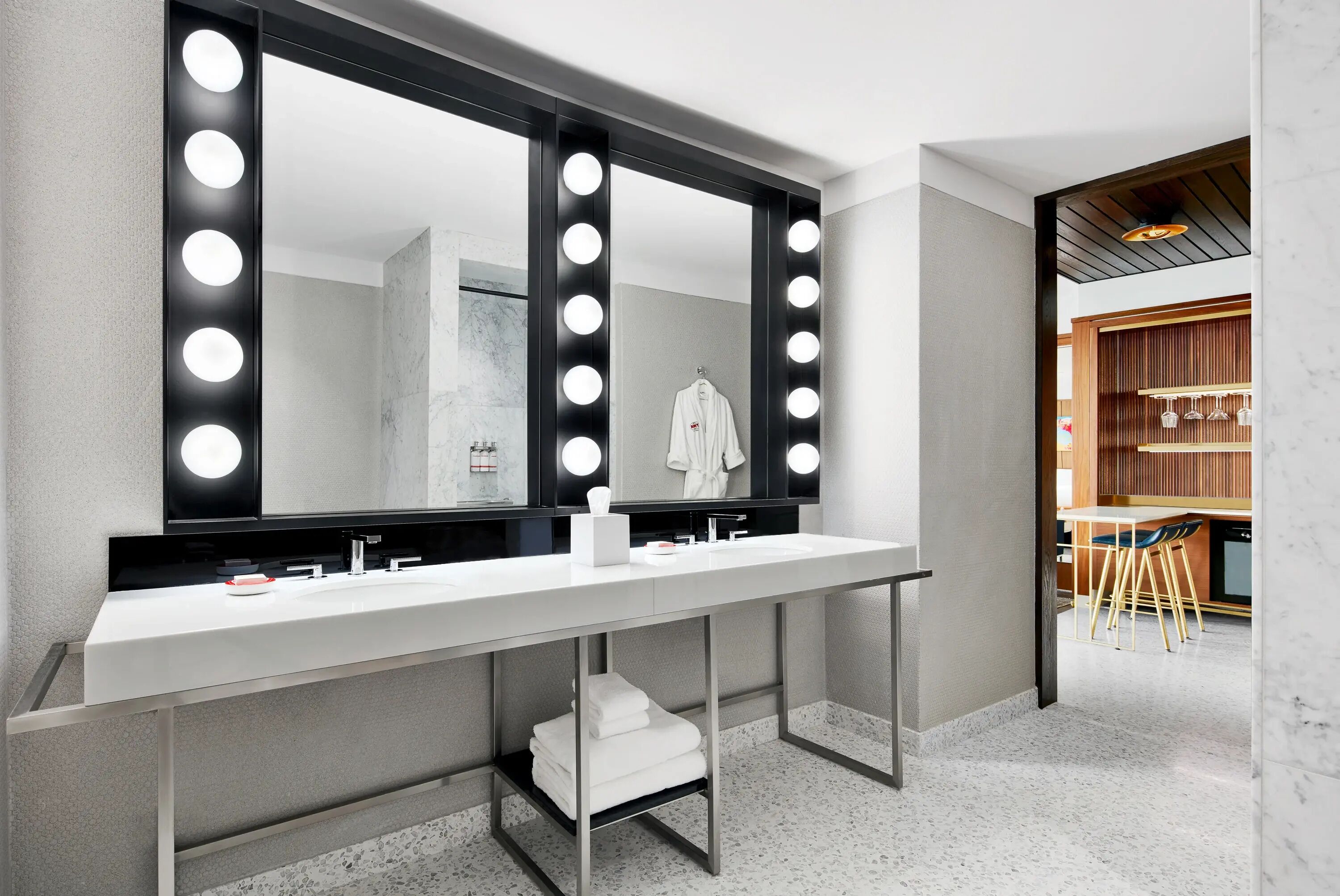 A modern bathroom with a large vanity mirror, two sinks, and a towel rack.