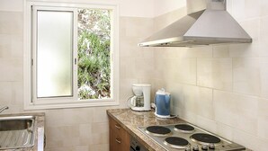 Une cuisine compacte avec une fenêtre, une cuisinière, une machine à café et une bouilloire.