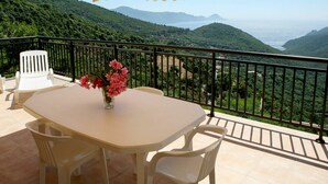 Un balcon avec une table, des chaises, un vase de fleurs et un auvent jaune à rayures.