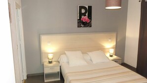 A bedroom with a large bed, two bedside tables with lamps, a wall-mounted light fixture, and a framed picture above the bed. - Nice apartment for 4 people with A/C, WIFI, TV, patio, pets allowed and panoramic view (Partinello)