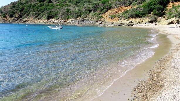 A beach with clear water, a boat, and a rocky hillside. - Nice apartment for 4 people with A/C, WIFI, TV, patio, pets allowed and panoramic view (Partinello)