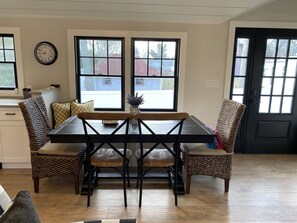 Un comedor con una mesa y sillas de madera, dos ventanas y un reloj en la pared.
