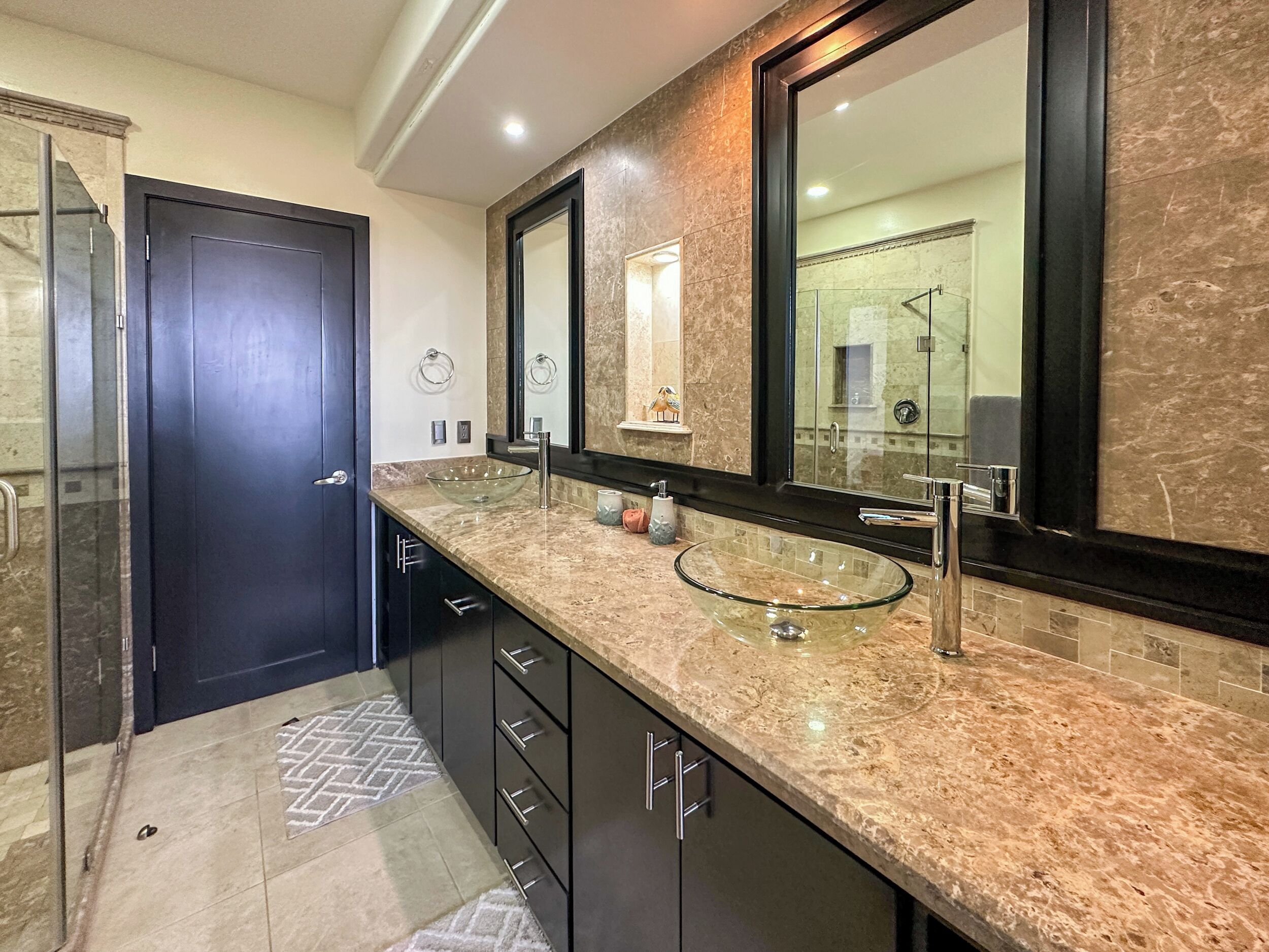 Une salle de bain moderne avec un lavabo en forme de bol en verre, des meubles de rangement aux couleurs sombres et un grand miroir.
