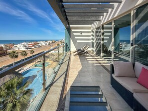 Een balkon met uitzicht op zee, een zwembad en een zithoek met kussens.