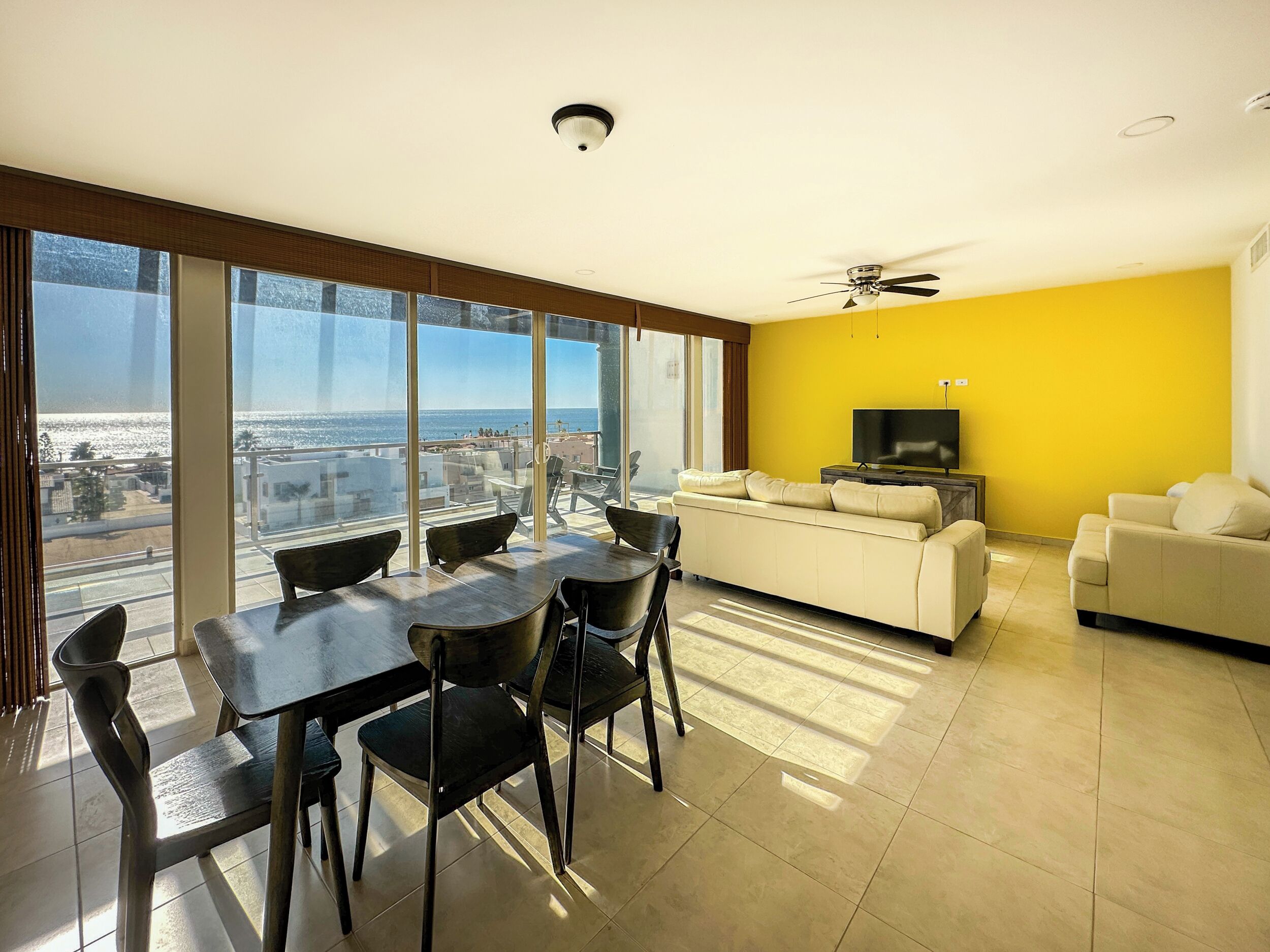 A modern living room with a large window, a sofa, a TV, and a dining area with chairs and a table.
