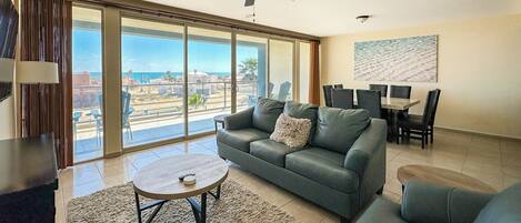 A spacious living room with a large sofa, a coffee table, and a dining area with chairs and a table.