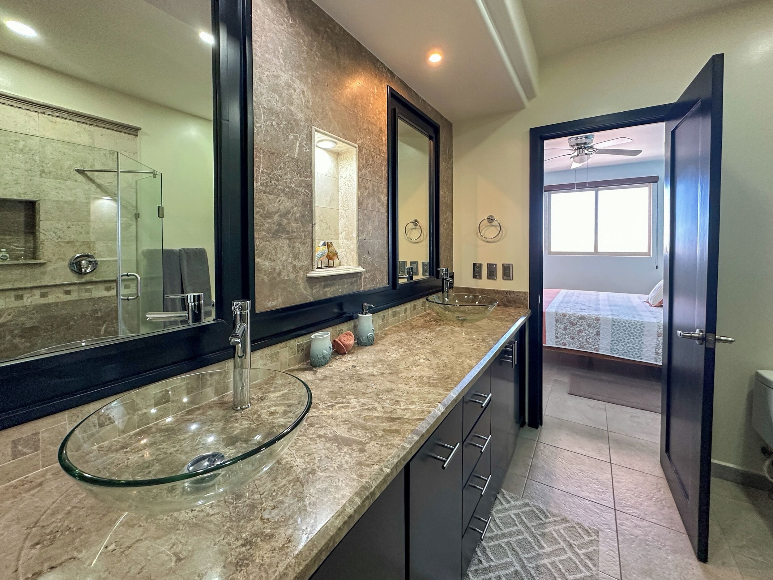 A modern bathroom with a glass sink, marble countertop, and a large mirror.