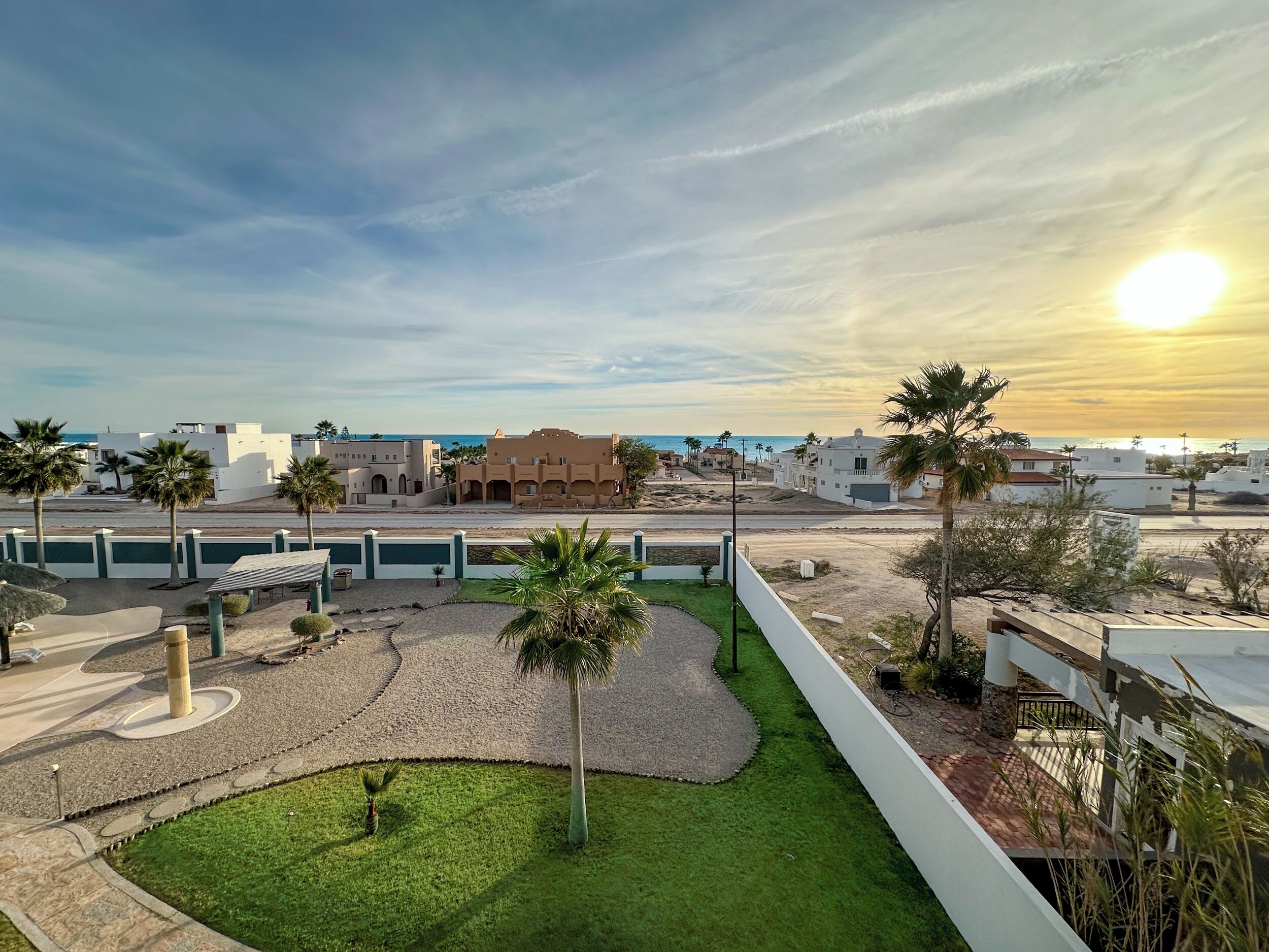 Quartiere residenziale con prato curato, palme e vista libera sul mare.
