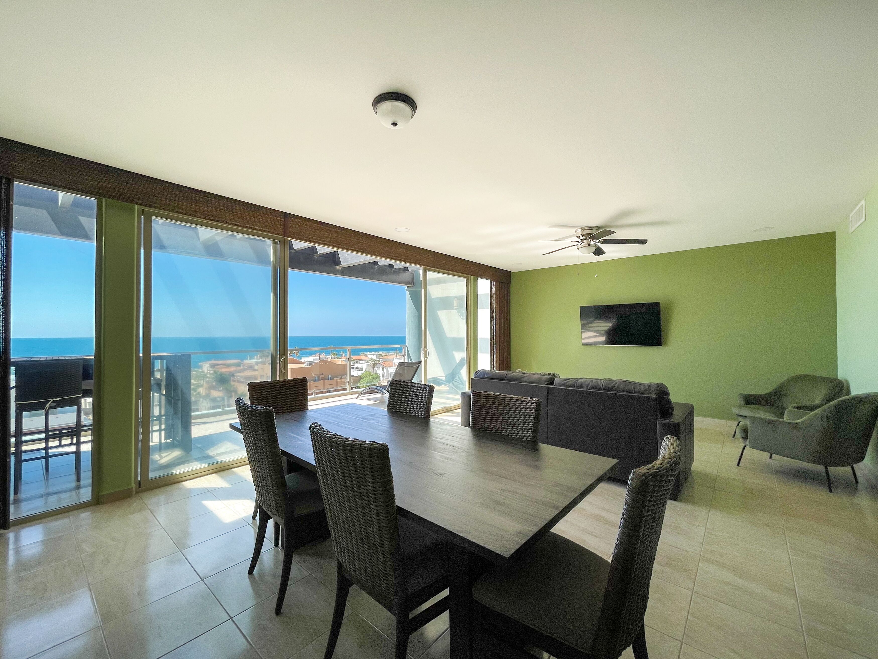 A spacious room with a large dining table, chairs, a sofa, and a TV on the wall.