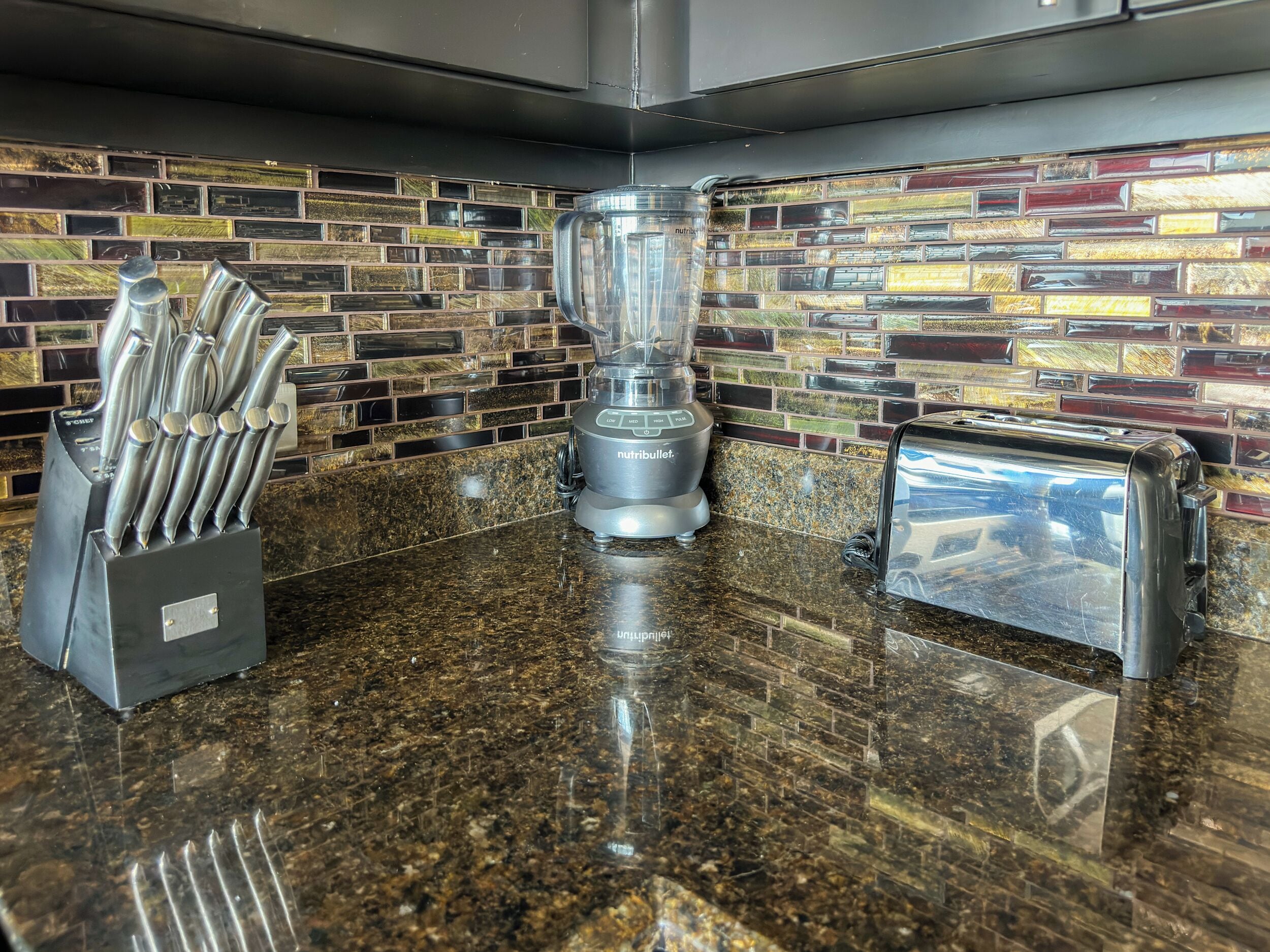 A kitchen with a granite countertop, a blender, a toaster, and a knife block.