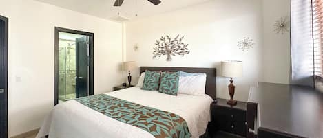 A bedroom with a bed, a ceiling fan, a nightstand, a dresser, and a door leading to a bathroom.