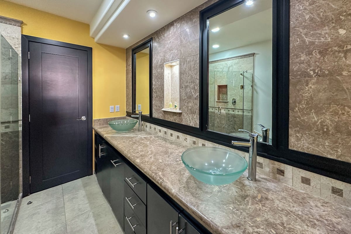 Un baño moderno con un lavabo de vidrio grande, muebles oscuros y un espejo amplio.