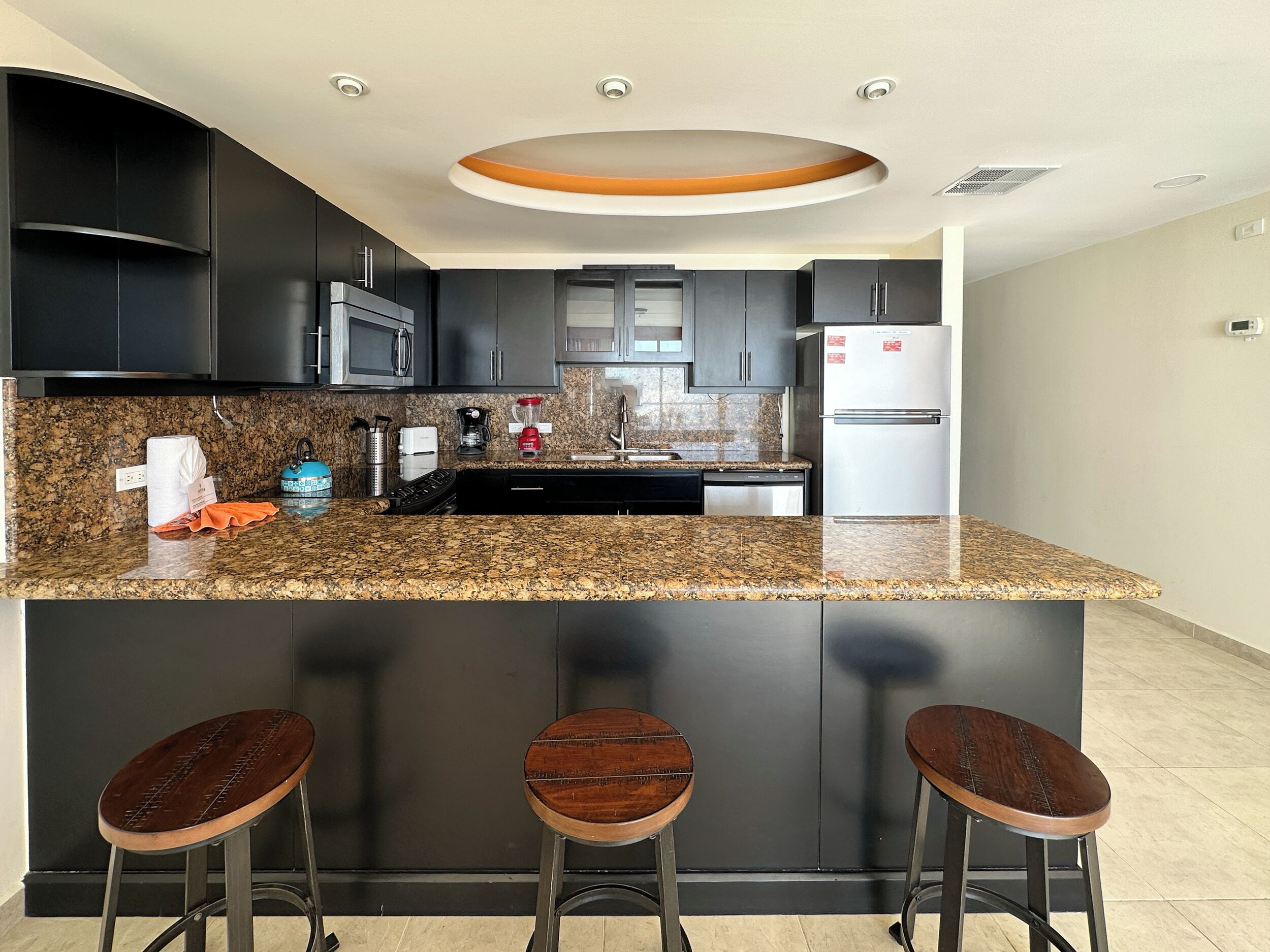 Eine moderne Küche mit dunklen Schränken, einer Granit-Arbeitsplatte, einem Einbauofen und einem Edelstahl-Kühlschrank.