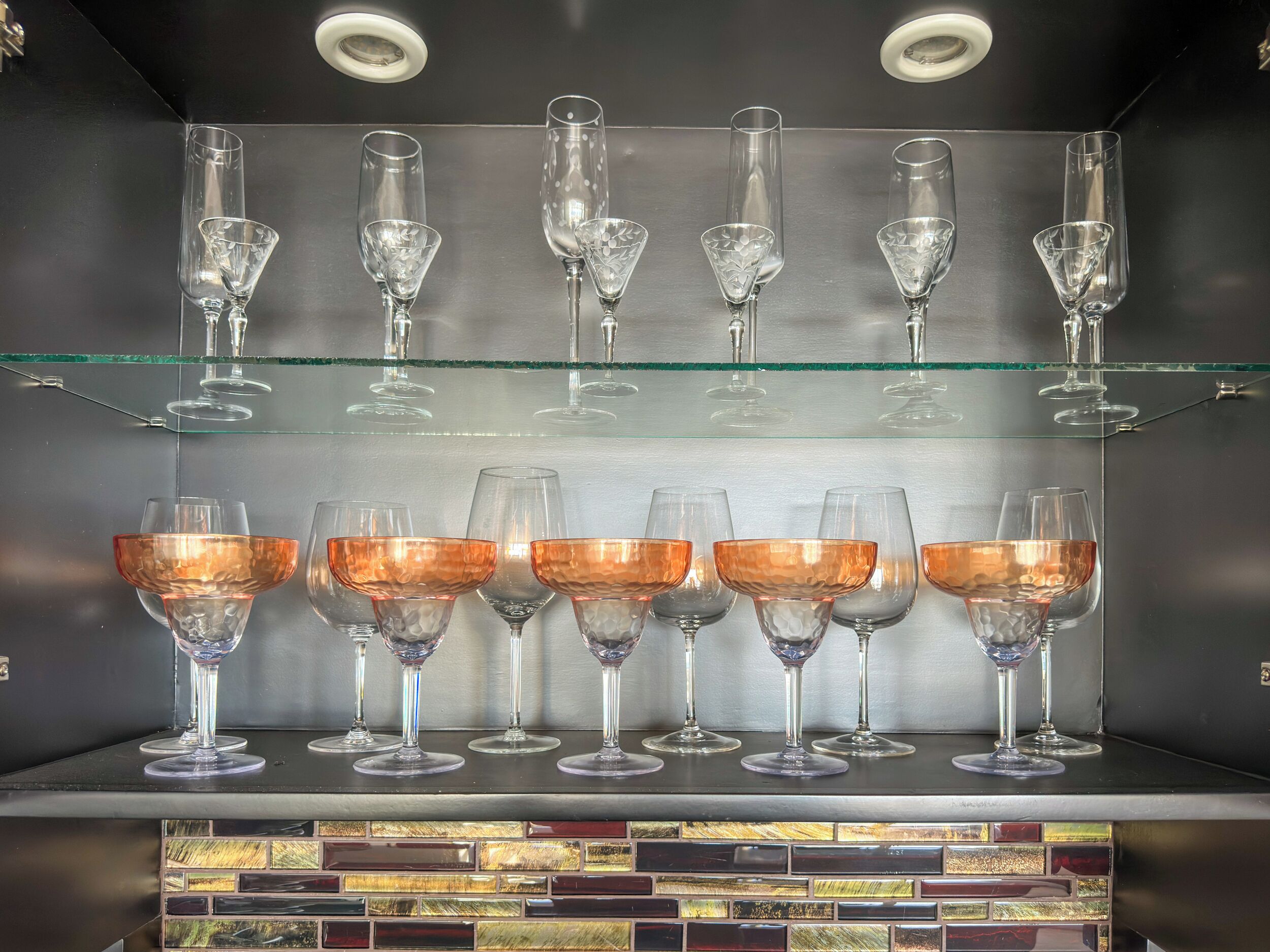 A bar area with multiple shelves displaying various types of glasses, including wine glasses and cocktail glasses.