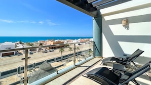 Ein Balkon mit Blick auf Strand und Stadt, mit Liegestühlen und einer Struktur mit Reetdach.