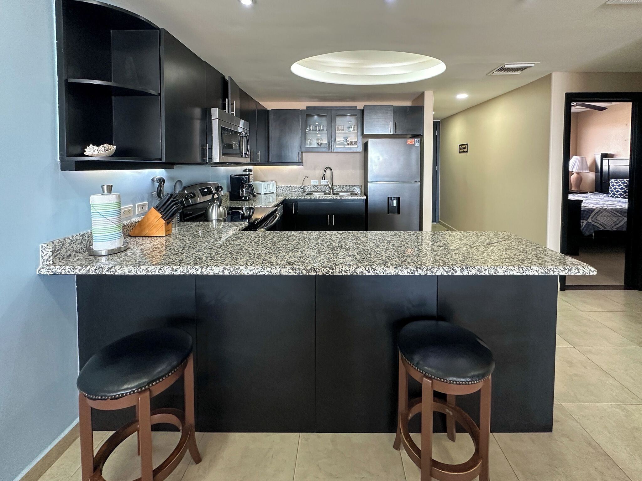 A modern kitchen with a granite countertop, stainless steel appliances, and two bar stools.
