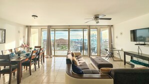 Ein geräumiges Wohnzimmer mit Essbereich, große Schiebeglasfenster, die auf einen Balkon mit Meer- und Stadtblick führen.