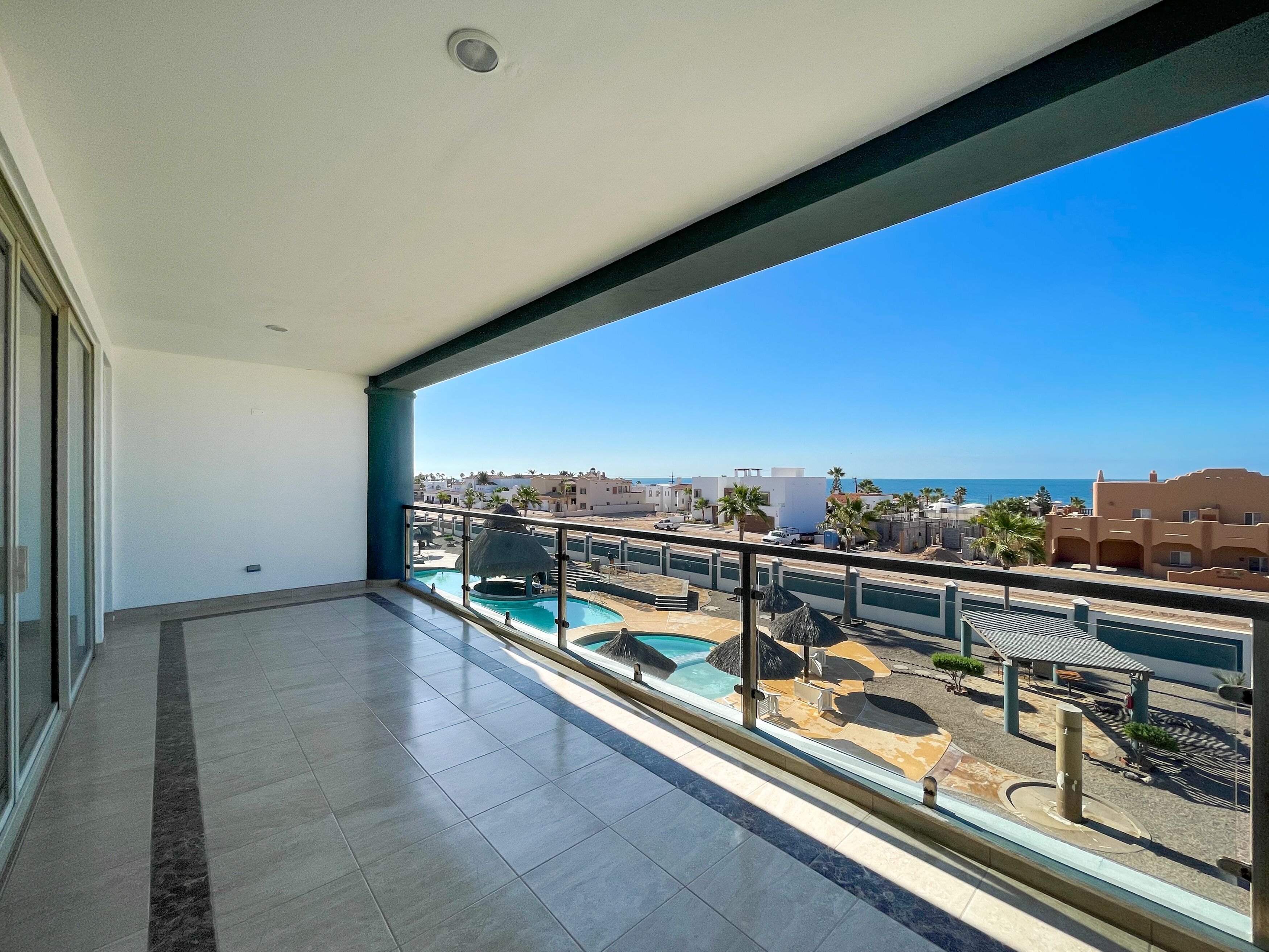 A balcony with a view of a swimming pool, palm trees, and buildings in the distance.