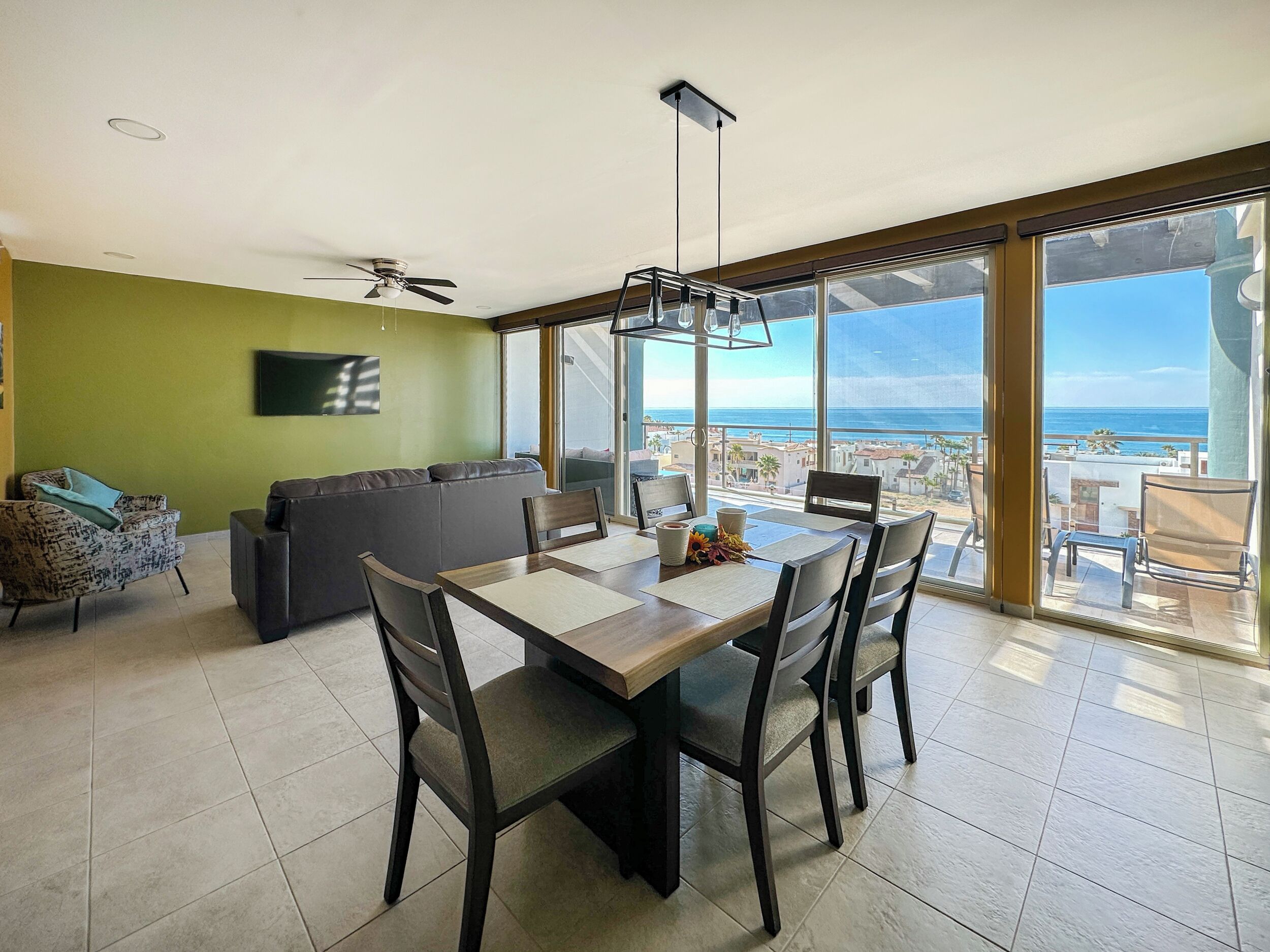 A dining area with a table and chairs, a sofa, and a TV on the wall.