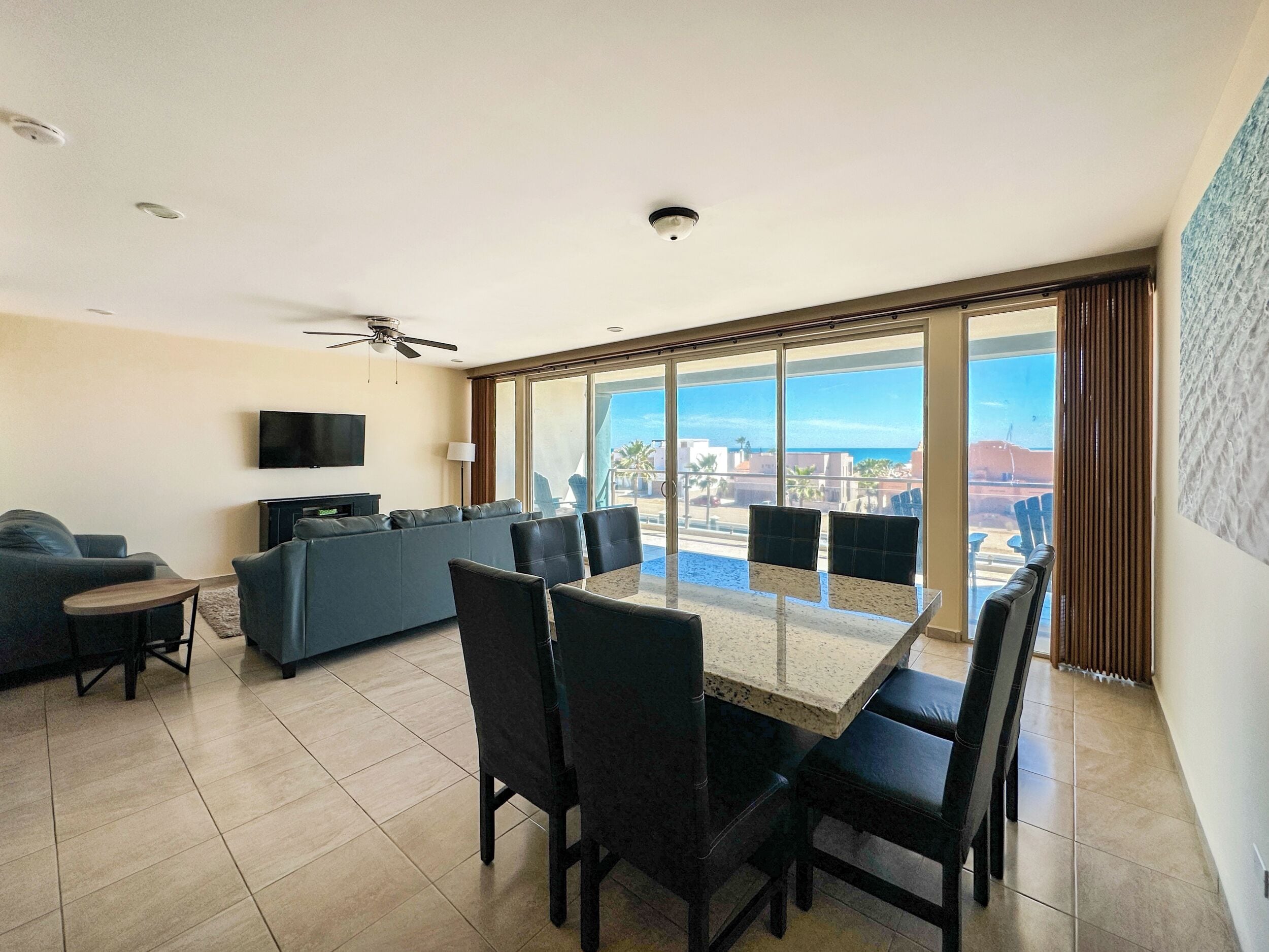 Amplia sala de estar con balcón, televisor de pantalla plana, sofá y mesa de comedor con sillas.