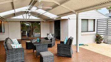 Een terras buiten met rieten meubilair, een plafondventilator en uitzicht op het huis.