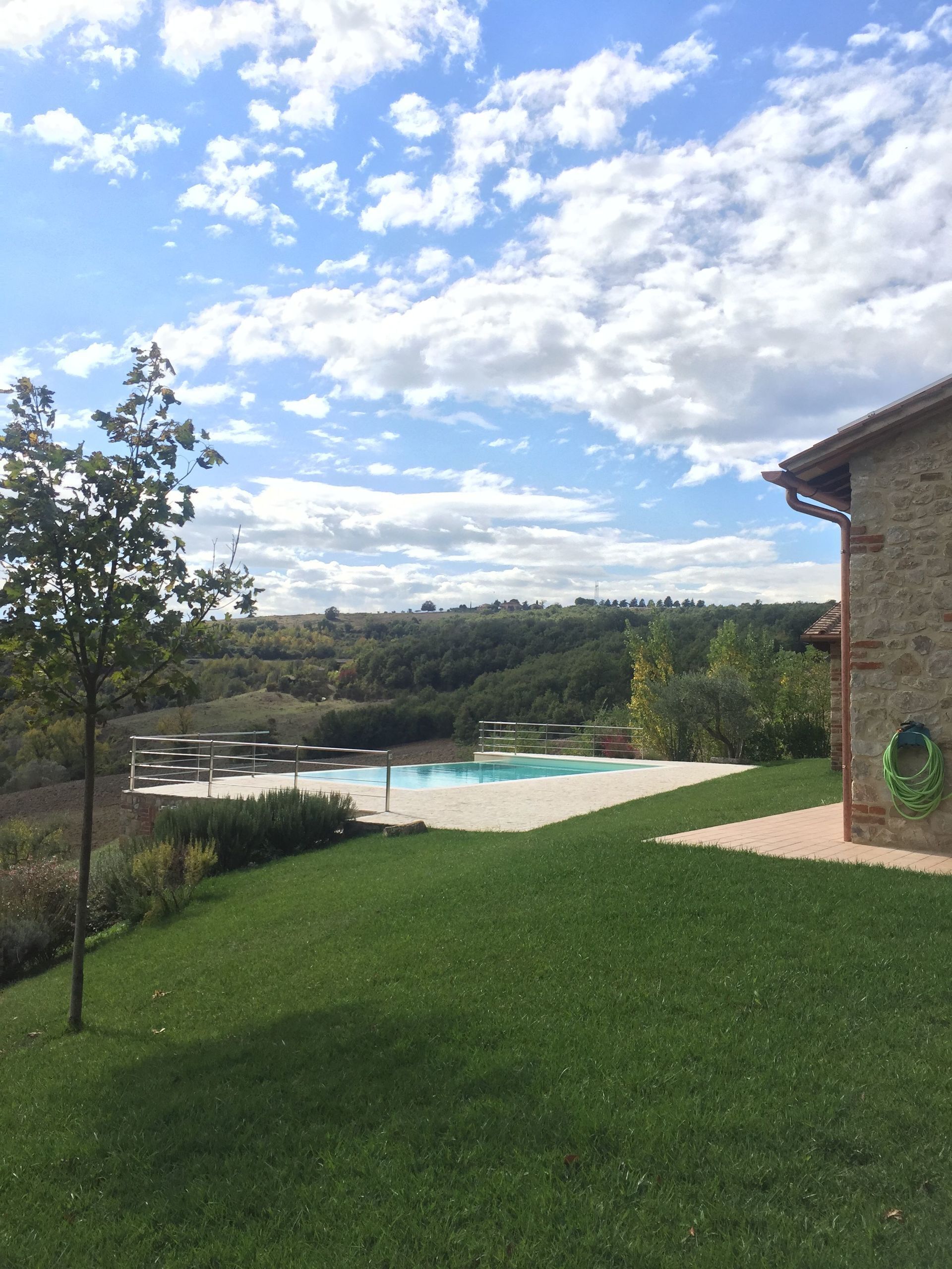 Una piscina con muelle de madera, rodeada de césped y un edificio de piedra.