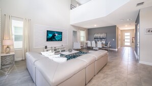 A spacious living room with a large L-shaped sectional sofa, a flat-screen TV mounted on the wall, and a dining area with white chairs and a table. - (AG2770) Storey Lake VILLA 5/5, Private Pool & Free Waterpark (Kissimmee)