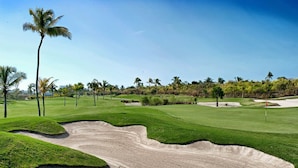 En golfbana med sandbunkrar, palmer och en klar himmel.