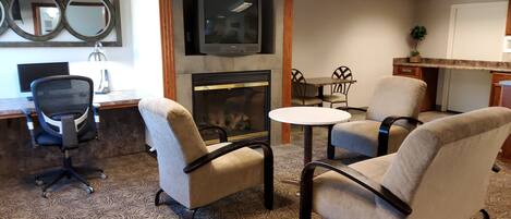 A hotel room with a fireplace, comfortable seating, a flat-screen TV, and a desk with a computer.