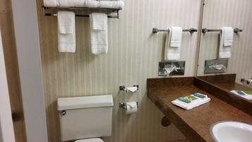 A bathroom with a toilet, sink, and mirror. There are towels hanging on a rack and a towel dispenser.