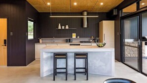 A modern kitchen with a central island, bar stools, and a large window. - Artisan Gunyulgup—Luxe Lakeside Wellness Hideaway (Yallingup)