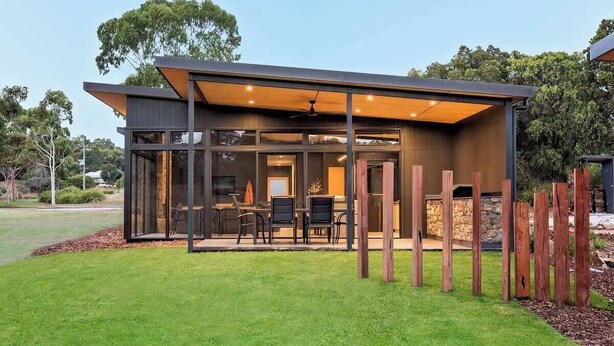 A modern house with a covered patio, large windows, and a stone fireplace. - Artisan Gunyulgup—Luxe Lakeside Wellness Hideaway (Yallingup)