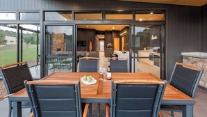 An outdoor dining area with a wooden table and chairs, a stone wall, and a view of the interior. - Artisan Gunyulgup—Luxe Lakeside Wellness Hideaway (Yallingup)