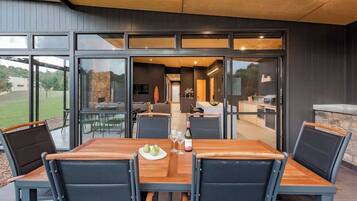 An outdoor dining area with a wooden table and chairs, a stone wall, and a view of the interior.