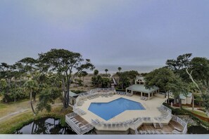 Zona de piscina con vistas al océano, rodeada de árboles y una terraza con sillones reclinables.