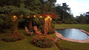 A garden with a pool, chairs, and a pergola with string lights. - Private rainforest villa nestled in the cool mountains of El Valle de Antón.. (Anton Valley)