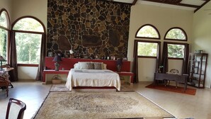 A bedroom with a stone wall, a bed, a desk, and large windows. - Private rainforest villa nestled in the cool mountains of El Valle de Antón.. (Anton Valley)