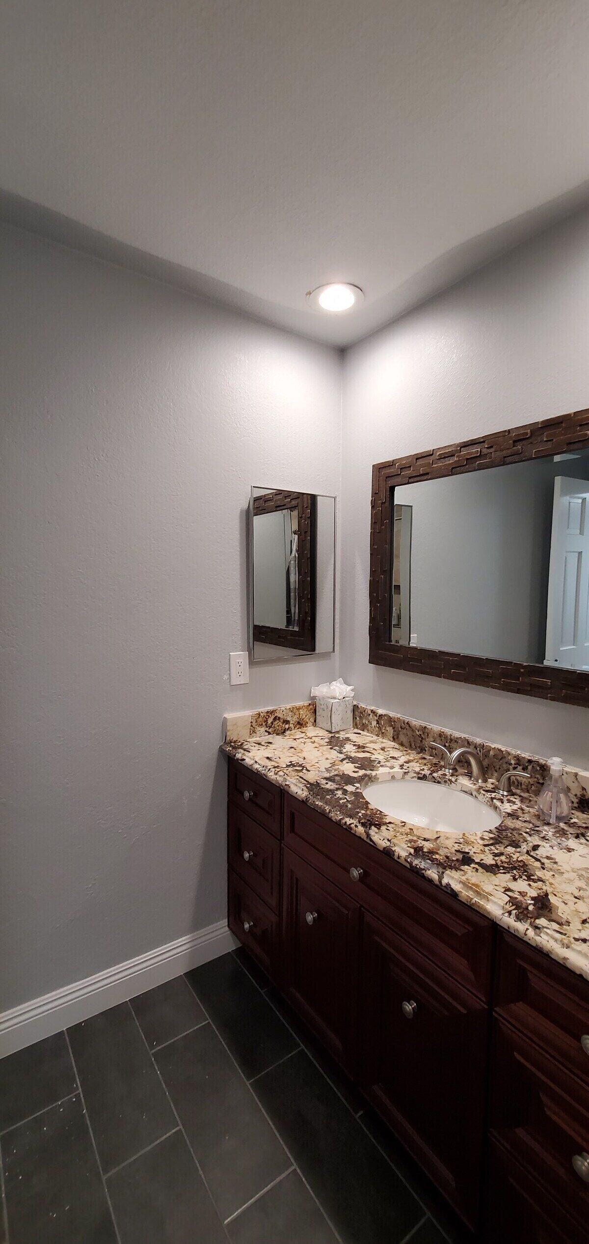 A bathroom with dark wooden cabinets, a marble countertop, and two mirrors.