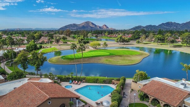 Un campo da golf con un lago, circondato da edifici residenziali e palme.