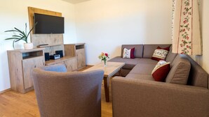Uma sala de estar moderna com sofá, poltrona e uma televisão de tela plana fixada em uma parede de madeira.