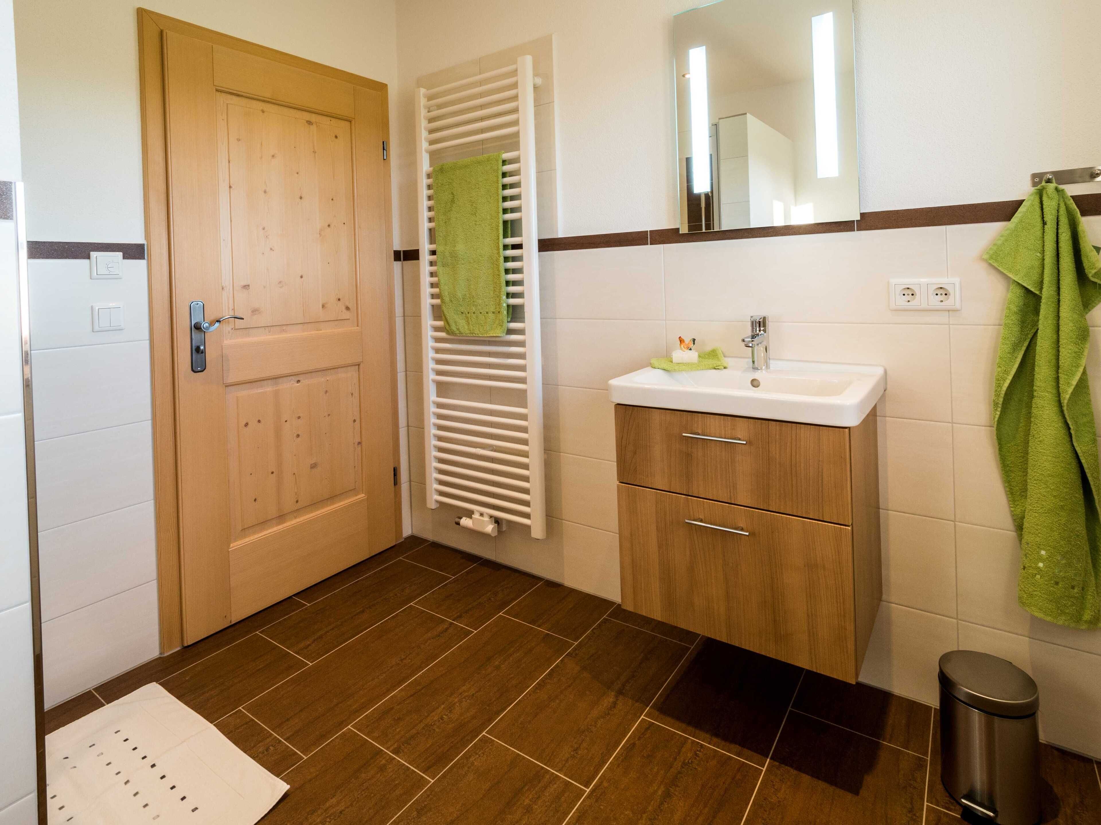 Une salle de bain avec une porte en bois, un porte-serviettes avec une serviette verte, un lavabo avec un porte-savon et une poubelle.