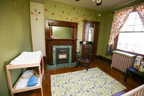 A room with a wooden crib, a fireplace with a green mantle, a patterned rug, and a window with floral curtains. - Large, kid friendly, private home on a brick street, 10 mins from downtown (Pittsburgh)