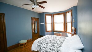 Ein Schlafzimmer mit Bett, Deckenventilator, Holzboden und einem Fenster mit Jalousien.