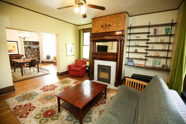 A living room with a fireplace, a sofa, a coffee table, and a dining area with chairs. - Large, kid friendly, private home on a brick street, 10 mins from downtown (Pittsburgh)