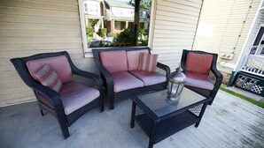 Eine Veranda mit Korbmöbeln, darunter zwei Stühle und ein kleiner Tisch, sowie einer Laterne.