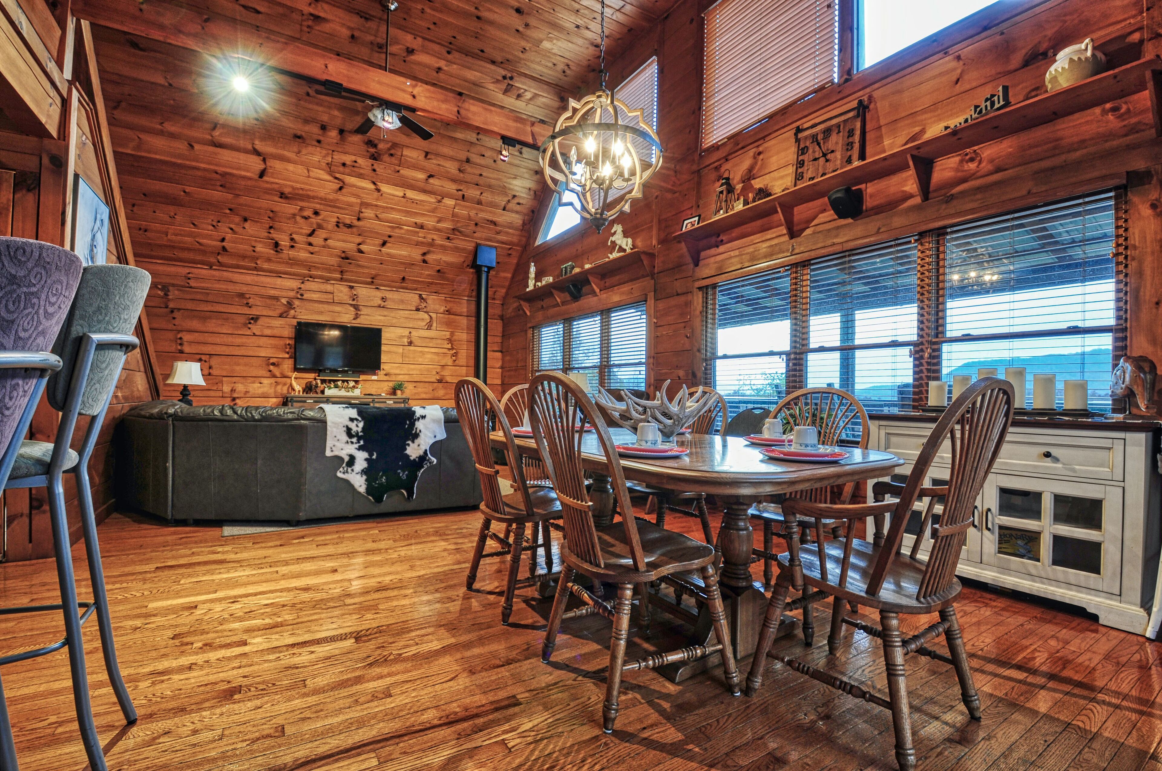 L’intérieur d’un chalet en bois comprend une table à manger, des chaises, un téléviseur et une grande fenêtre.